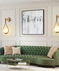 Mid Century Drop Design Wall Sconce In Brushed Brass, Two Pack, illuminating living room with green sofa and wall art.