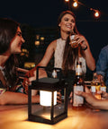 Outdoor Table Lamp With Bright LED Light in use on patio, people gathered around, bottle on table, solar lantern illuminates night.