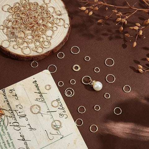 150 Pcs 14K Gold Filled Twisted Open Jump Rings with pearl pendant on brown surface, 6mm, 8mm, 10mm sizes for jewelry making.
