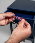 Hands holding a tube of Tough As Nails Medium Strength Threadlocker Glue Secures Nuts Bolts And Fasteners Against Shake Out Vibrations Rusty Threads Removable Formula 12 Pack Of 6 Ml Tubes.