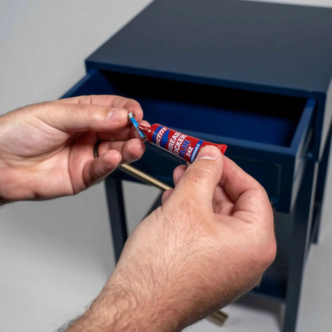 Hands holding a tube of Tough As Nails Medium Strength Threadlocker Glue Secures Nuts Bolts And Fasteners Against Shake Out Vibrations Rusty Threads Removable Formula 12 Pack Of 6 Ml Tubes.