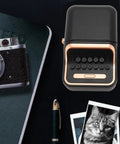 Cool Retro Label Printer With Bluetooth 5.0 Connectivity And Compact Design Perfect For Home Office Organization Tasks Features Inkless Thermal Printing Technology Compatible With A Range Of Paper Widths From Thirty Two Millimeters To Fifty Two on a desk with a vintage camera.