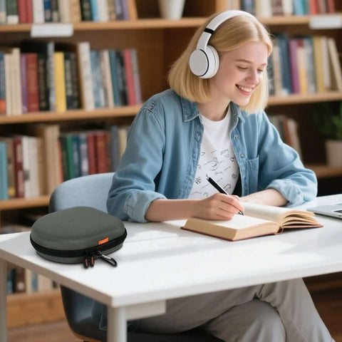 Heavy Duty Hard Shell Headphone Case on a table beside a student studying, 8.7x8.3 inch dark green case with quick release clip.