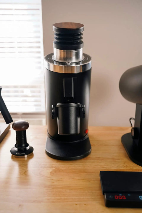 Heavy Duty 64Mm Flat Burr Electric Coffee Grinder Designed For Single Dosing Habits With Anti Popcorn Guard And Zero Static Hiccups grinding on a wooden table.