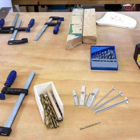 Workshop table with 24 Piece Drywall Toggle Anchors And Screws Kit, clamps, drill bits, and wooden blocks visible.