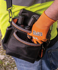 Worker wearing an orange glove handling tools in a tool pouch.