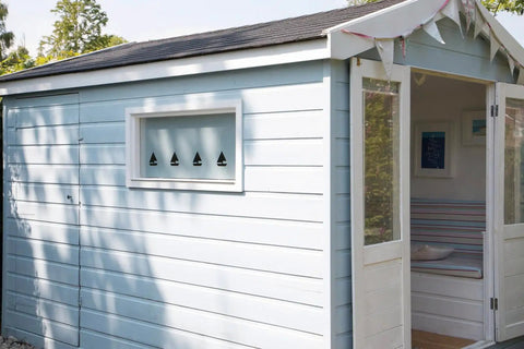 Light blue shed with row of triangular cutout designs on window, open door showing interior decor.