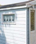 Light blue wooden shed with open doors, displaying a nautical-themed interior, small triangular window cutouts visible, surrounded by trees.