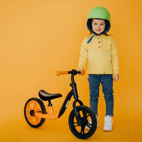 Child standing beside orange balance bike with Kid Bike Seat Replacement Cushion for 12 and 14 Inch Balance Bikes visible, black.