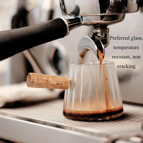 Double Scale Glass Measuring Cup With Wooden Handle For Coffee And Espresso, Milk Frother, V-Shaped Glass Cup, Borosilicate Heat Resistant, Easy Pour And Precise Measurements For Home Barista being filled with espresso from a machine.