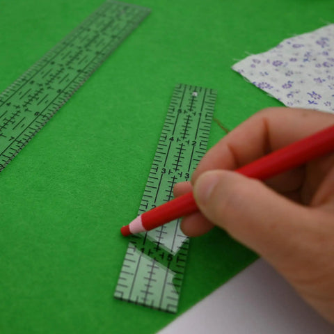 Hand using a red pencil on a green felt background with Dead Simple Acrylic Quilting Rulers And Nifty Fabric Cutting Templates For Patchwork Projects.