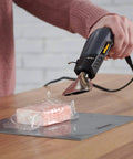 All In One Dual Temperature Electric Heat Gun Kit HT400 680F And 450F being used for shrink wrapping on a wooden table.