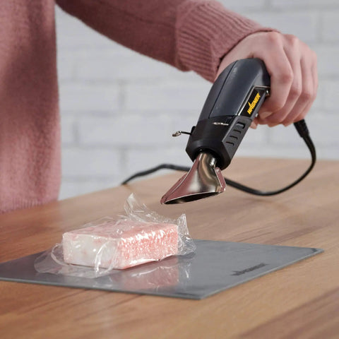 All In One Dual Temperature Electric Heat Gun Kit HT400 680F And 450F being used for shrink wrapping on a wooden table.