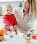 Mother feeding baby using Glass Baby Food Storage Jars 4 Oz 12 Pack With Color Lids Totally Leak Proof BPA Free Reusable Containers