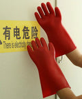 Hands wearing Heavy Duty Electrical Insulated Gloves Class 00 12KV 1.8mm Thick Rubber touching a warning sign.