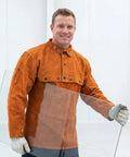 Man wearing Leather Welding Jacket With Cape Sleeves And Bib Apron Top Notch Pro Grade Welder Safety Coat, holding glass pane.