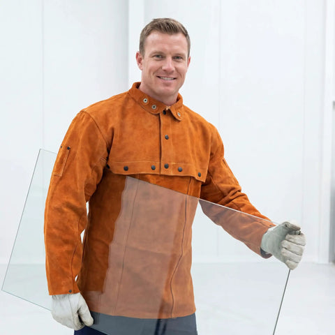 Man wearing Leather Welding Jacket With Cape Sleeves And Bib Apron Top Notch Pro Grade Welder Safety Coat, holding glass pane.