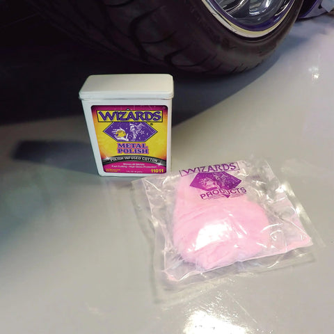 Front view of Wizards Metal Polish tin (3 oz) with a pink polishing cloth in a plastic bag beside a car wheel.