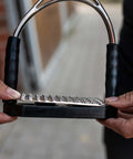 Close-up of 12cm stainless steel Bow Balance Stirrup Pads held by a rider, showing durable construction details