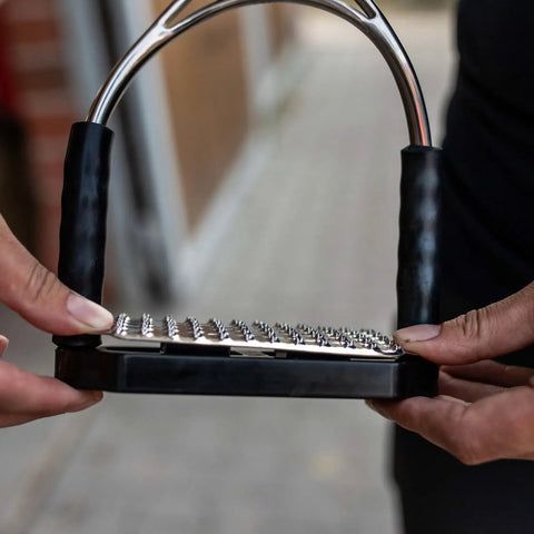 Close-up of 12cm stainless steel Bow Balance Stirrup Pads held by a rider, showing durable construction details