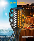 4 Pack 43 Inch Solar Torch Lights With 96 LEDs showing realistic flickering flame effect next to outdoor dining setup at night.