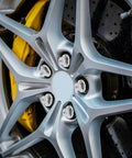 Five Piece Silver Steel Car Wheel Lug Nuts Set For Universal Tire And Rim Replacement Premium Rust Resistant Finish Bulletproof Hold No Drama Swap For Daily Drivers mounted on a silver alloy wheel with visible yellow brake caliper.