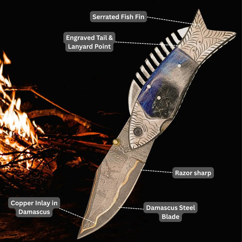 Fish Style Folding Knife With Ladder Pattern Damascus Blade And Blue Resin Handle in front of a campfire.
