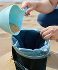 Filling Two Pack 45 Lbs Heavy Duty Umbrella Base Sand Bags with sand using scoop on beach