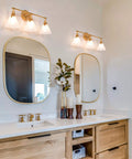 Three Light Gold Vanity Light Fixtures With White Frosted Glass Shades Over Mirror In Brushed Antique Gold Finish in bathroom