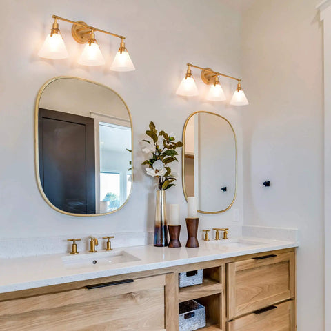 Three Light Gold Vanity Light Fixtures With White Frosted Glass Shades Over Mirror In Brushed Antique Gold Finish in bathroom