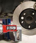 Digital Brake Caliper 0-150mm LCD Electronic Vernier Gauge measuring brake pad thickness next to a rotor in a garage