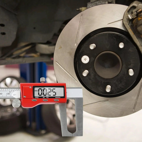 Digital Brake Caliper 0-150mm LCD Electronic Vernier Gauge measuring brake pad thickness next to a rotor in a garage