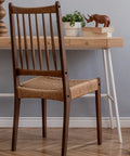 Wooden chair with woven seat in front of wooden desk with plant and decorative items