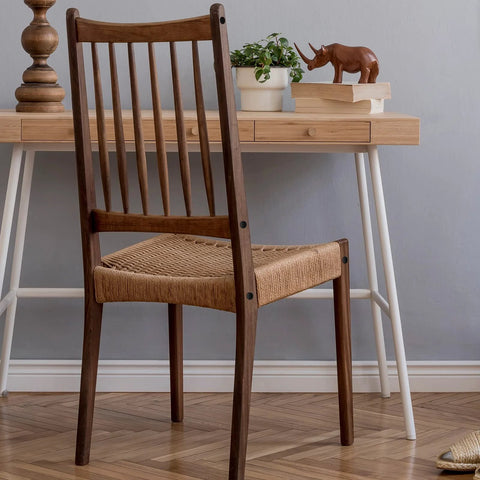 Wooden chair with woven seat in front of wooden desk with plant and decorative items