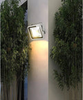 JUDYSSY Spot Lighting Led Flood Light Outdoor mounted on wall, illuminating with warm light, surrounded by greenery.