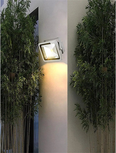 JUDYSSY Spot Lighting Led Flood Light Outdoor mounted on wall, illuminating with warm light, surrounded by greenery.