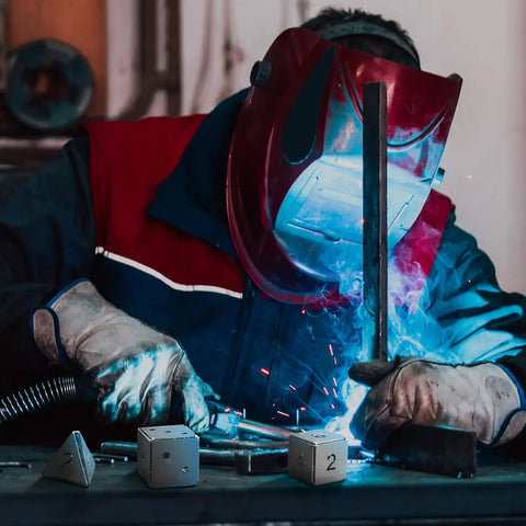 Welder using Three Style Aluminum Welding Coupon Set For One Point Five Inch Practice Plates, DIY Dice Shapes, Square And Triangle Coupons For TIG MIG Gas Arc Stick Welding Training, Beginner Friendly And Ready For Realistic Welding Practice, with dice-shaped aluminum pieces in front of him.