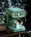 Green compact high pressure espresso machine with steam frother, on a countertop, surrounded by pastries and coffee beans.