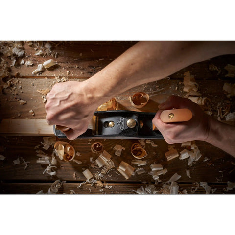 Hands using Low Angle Jack Plane, Sweetheart No 64 Style to flatten wood on workbench, wood shavings visible