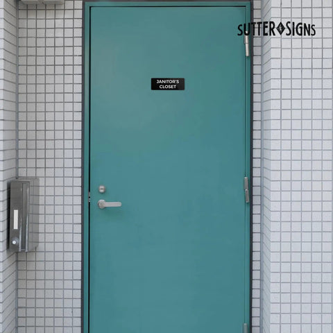 Durable ABS Door Sign With Full Adhesive Backing 2x6 Inch on a janitor closet door in a tiled wall, high visibility label