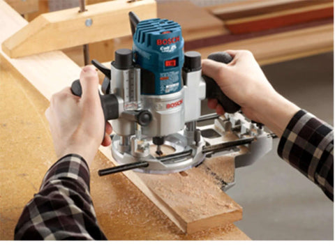 Front view of Bosch wood router with blue top and silver body, held by two hands over a wooden workbench.