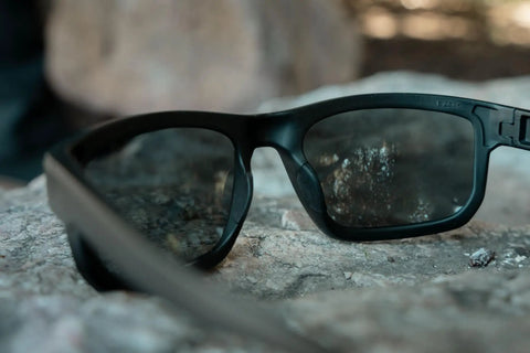 Kickass Z87 Certified Wayfarer Safety Sunglasses Featuring Hella Effective Antifog Smoke Lenses and Totally Shatterproof Matte Black Frames Built Tough For Male Workers resting on a rock.