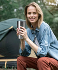 Woman holding a Hardcore 30oz Stainless Steel Tumbler Featuring Double Wall Vacuum Insulation outdoors by a tent.