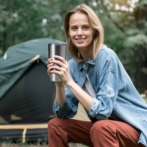 Woman holding a Hardcore 30oz Stainless Steel Tumbler Featuring Double Wall Vacuum Insulation outdoors by a tent.