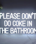 White neon sign with the text 'PLEASE DON'T DO COKE IN THE BATHROOM' on a gray wall.