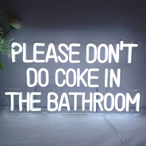 White neon sign with the text 'PLEASE DON'T DO COKE IN THE BATHROOM' on a gray wall.