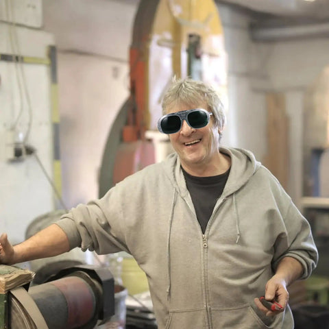 Man wearing Badass Welding Glasses With Anti Glare Black And Gray Lenses in workshop, smiling and working on projects.