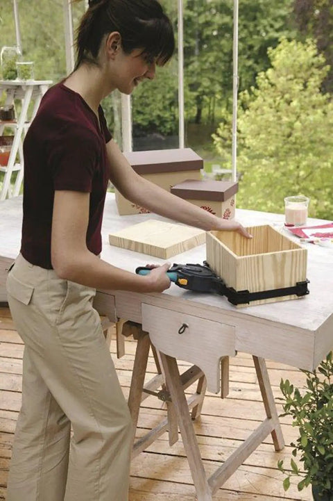 Person using One-Hand Ratcheting Band Clamp For Quick Glue-Ups And Framing, 16-Inch Clamp With Self-Adjusting Corners on wooden box.
