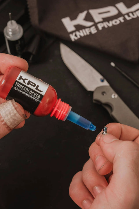 Applying Blue Thread Locker For Knife And Gun Pivot Screws Keep Your Gear Tight Oil Tolerant And Fast Curing Medium Strength 10ml Precision Screw And Part Retainer For Secure Yet Removable Fasteners onto a small screw, knife in background