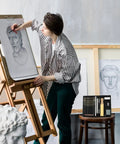Artist sketching with The Ultimate 22 Piece Sketch Pencils Set for Artists With Graphite Pencils From 6H To 10B, visible on stool.